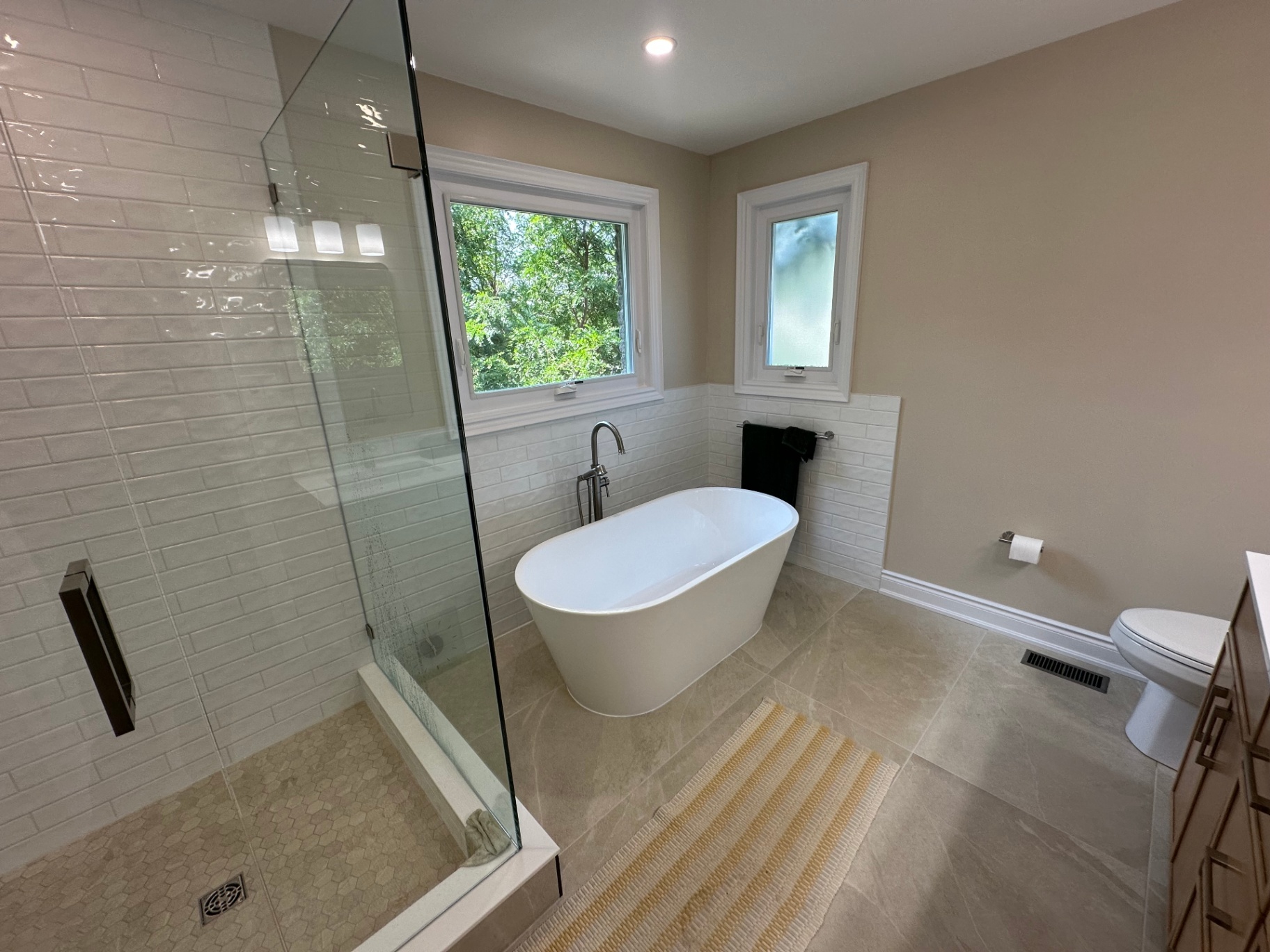 Bright finished bathroom with a freestanding tub and floor-mount filler beneath a window onto green trees