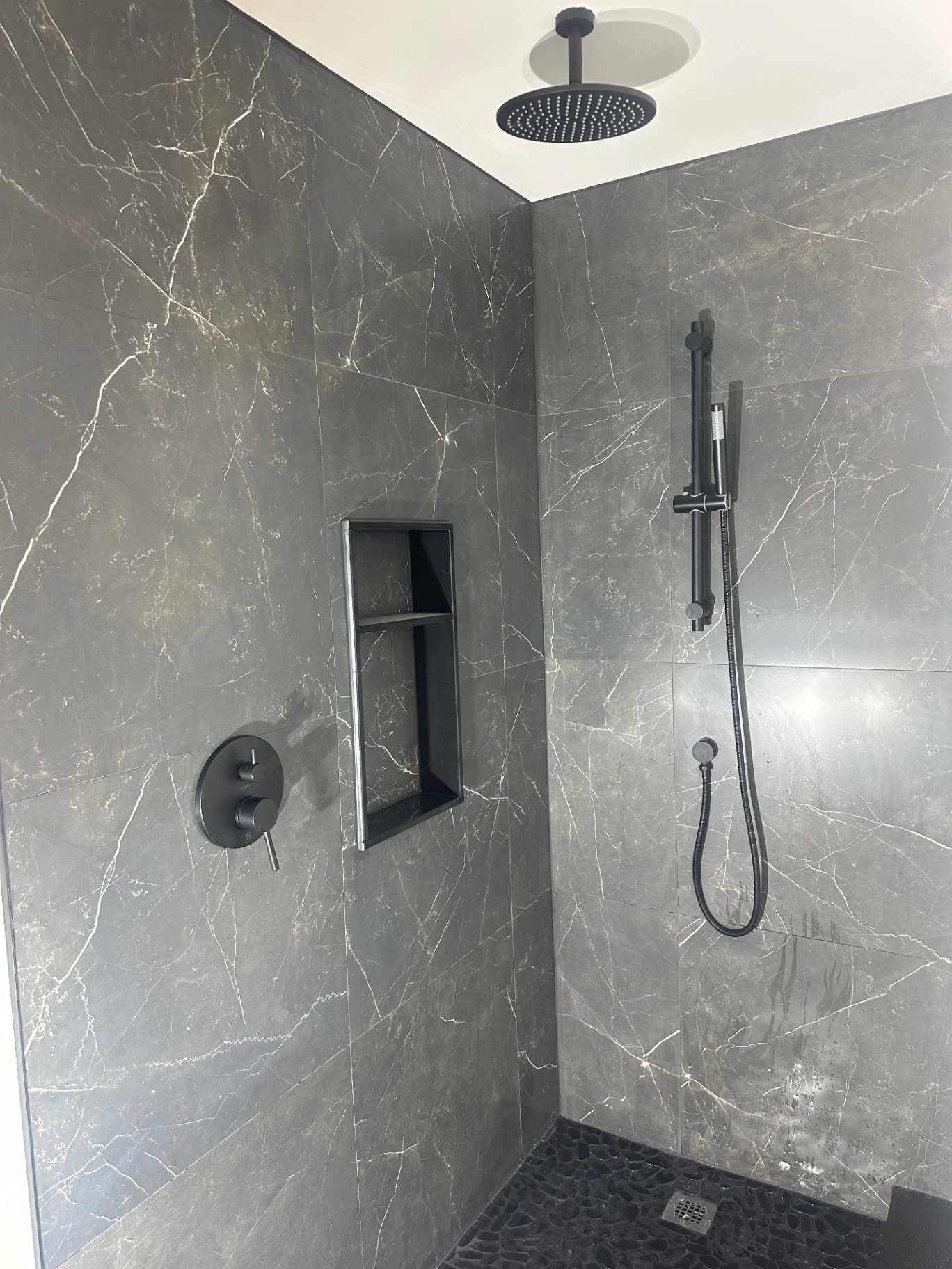 Dark marble-look shower with matte-black rain head, recessed valve trim and niche