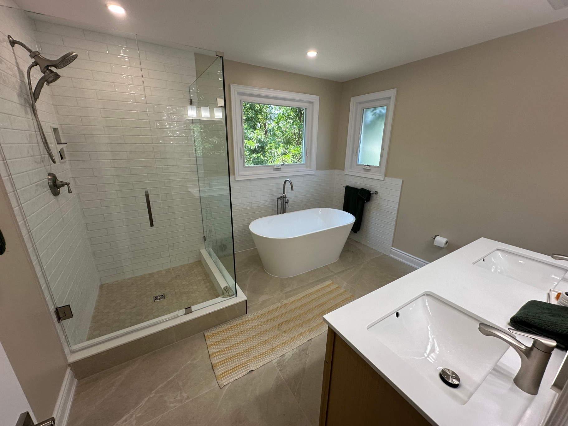 Finished main bathroom with freestanding tub, glass shower and double vanity faucets
